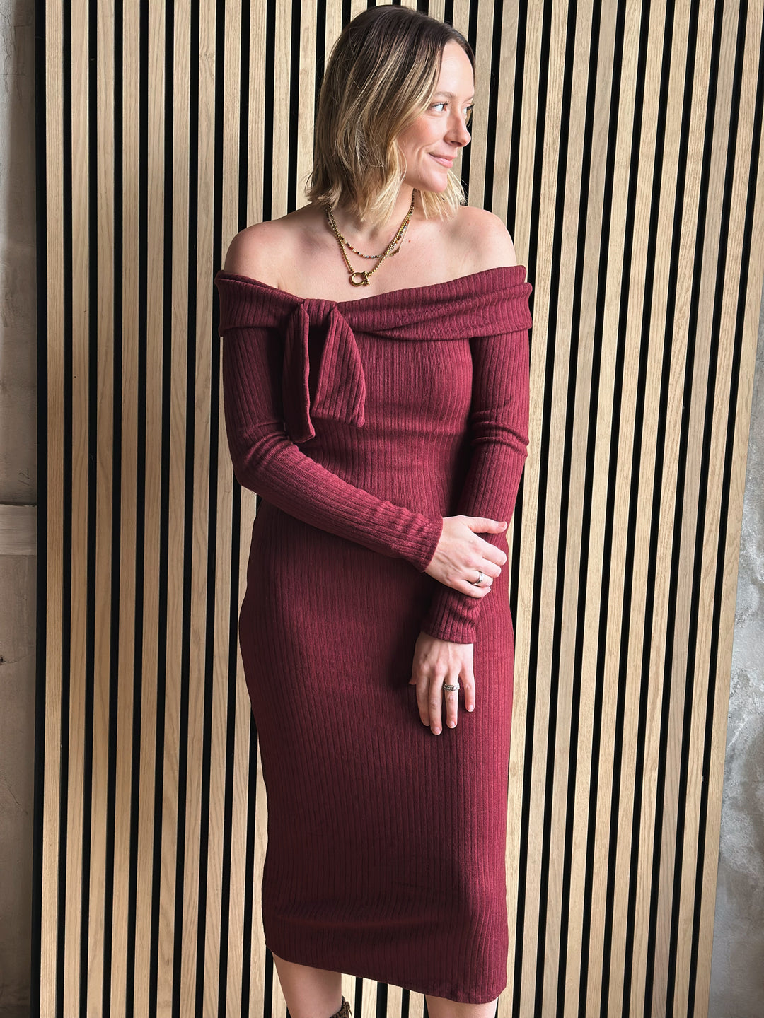 Woman wearing a burgundy off-shoulder dress against a striped wall.