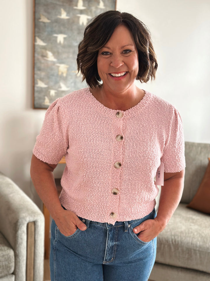 Woman wearing a pink textured cardigan and blue jeans.