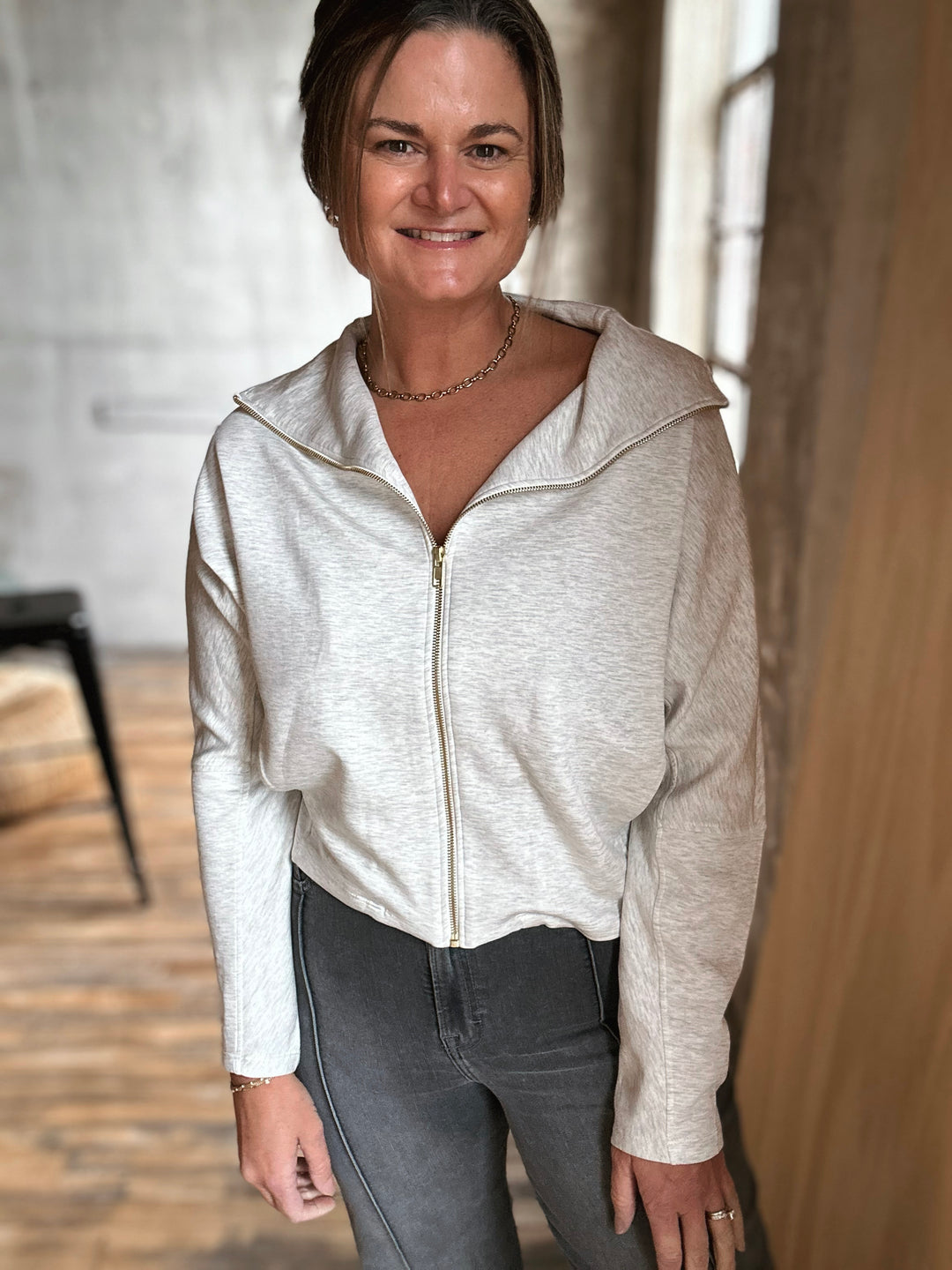 Woman wearing a light gray zip-up hoodie in an indoor setting