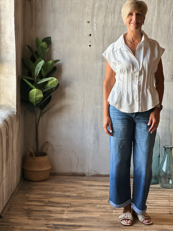 Woman standing in a room with a plant and wooden floor.