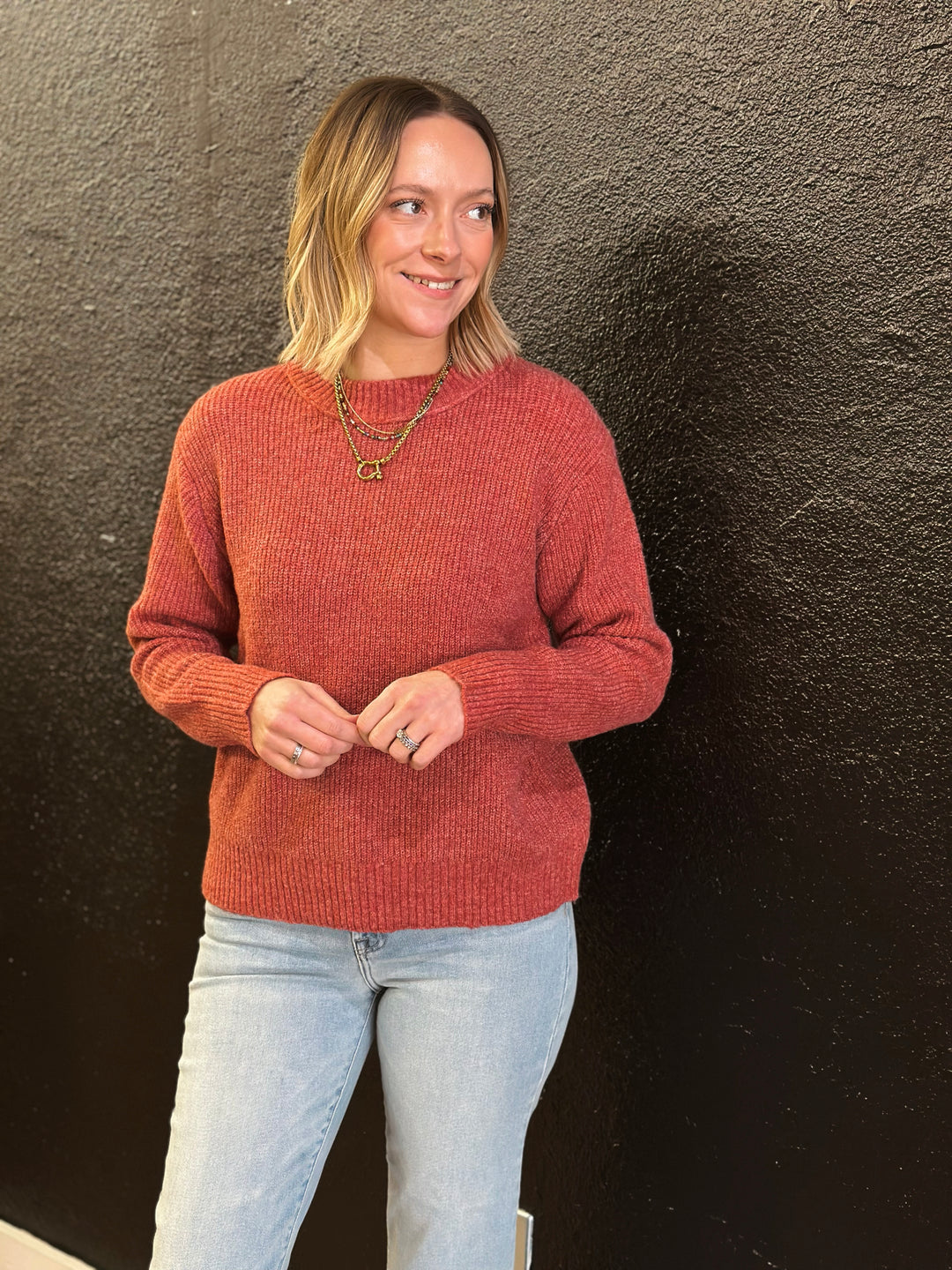 Woman wearing a red sweater and light blue jeans against a dark background