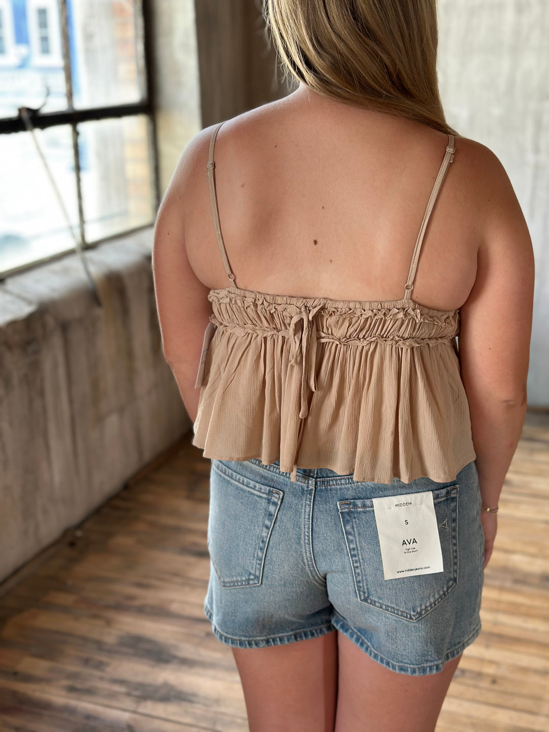 A person wearing a beige top and denim shorts indoors.
