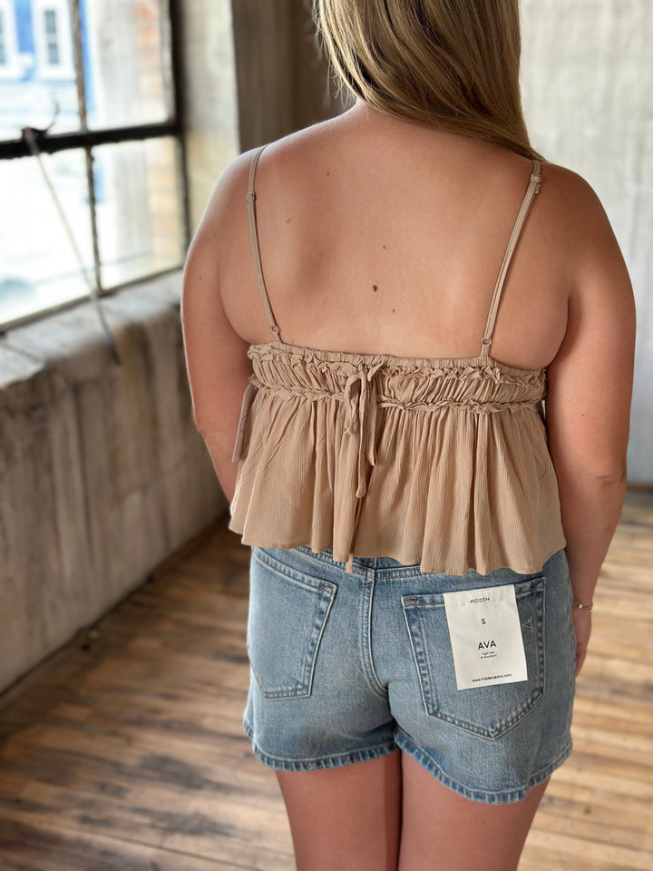 A person wearing a beige top and denim shorts indoors.