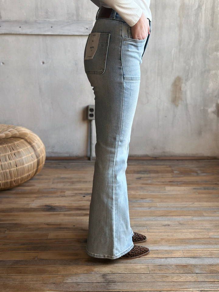 Person wearing light blue flared jeans standing in a room with wooden floor and textured walls.