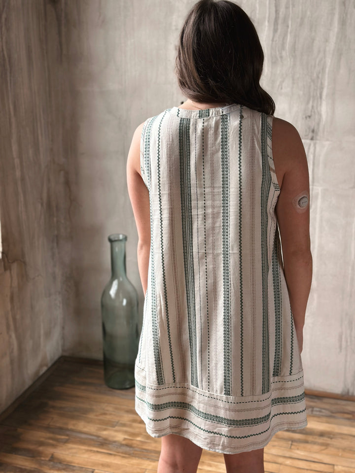 Person wearing a sleeveless dress with a striped  pattern in a room with a textured wall and wooden floor.
