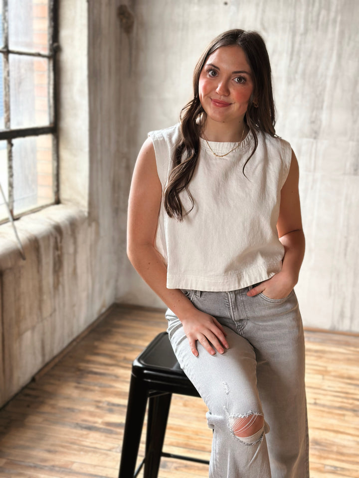 Woman wearing a white denim top in a room with wooden floor and large window