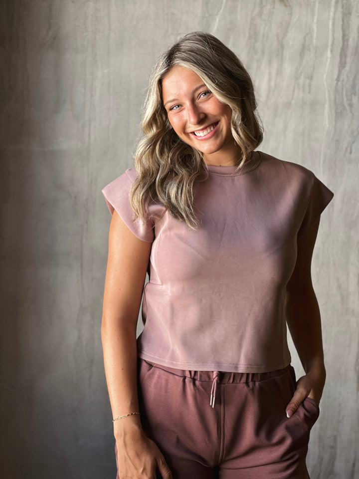 Woman wearing a mauve top and pants against a gray background