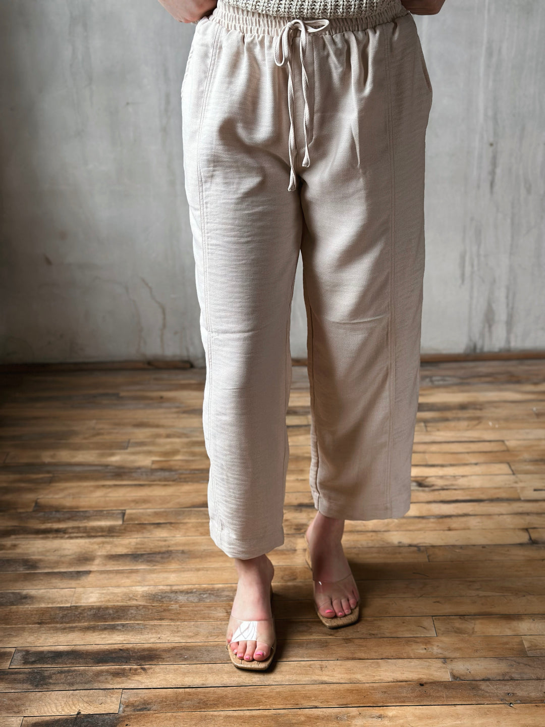 Person wearing beige pants standing on a wooden floor with a gray wall background