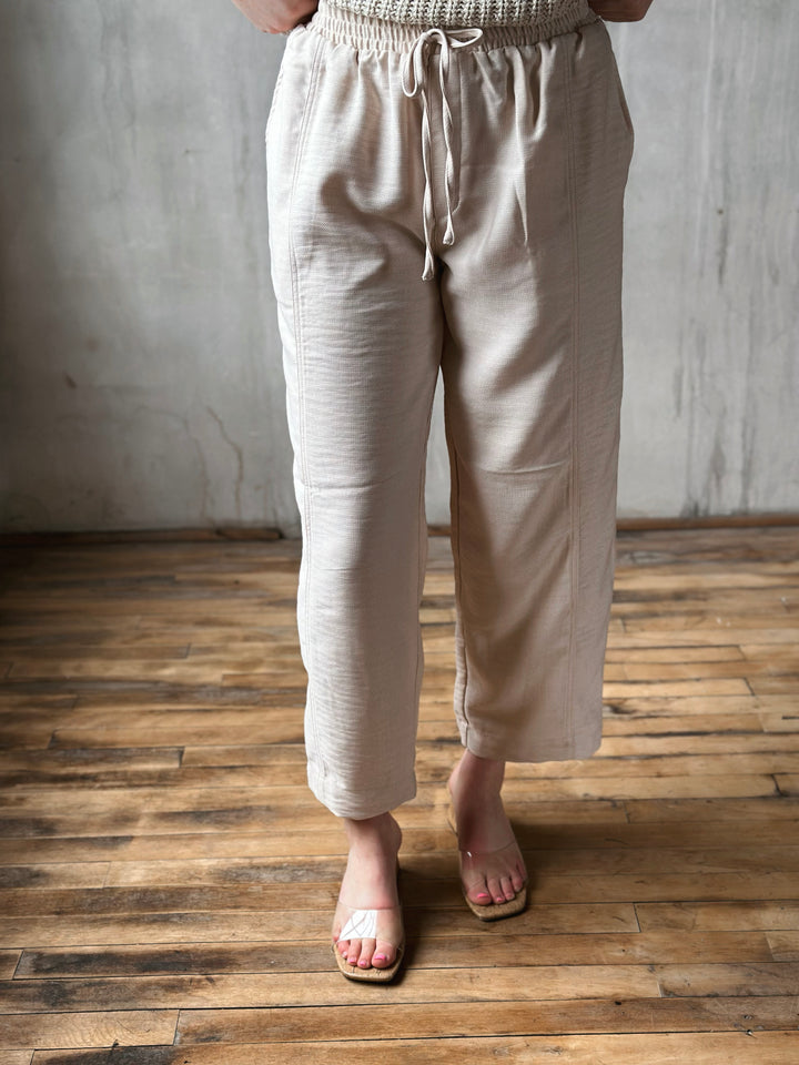Person wearing beige pants standing on a wooden floor with a gray wall background