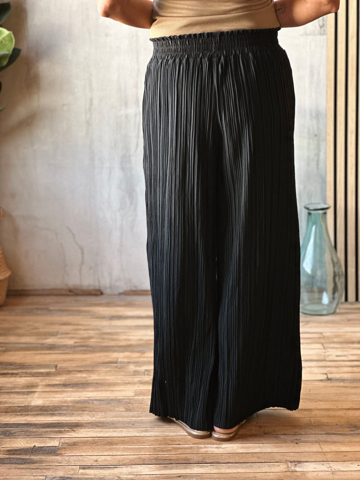 Person wearing a black pleated skirt on a wooden floor with a neutral wall background