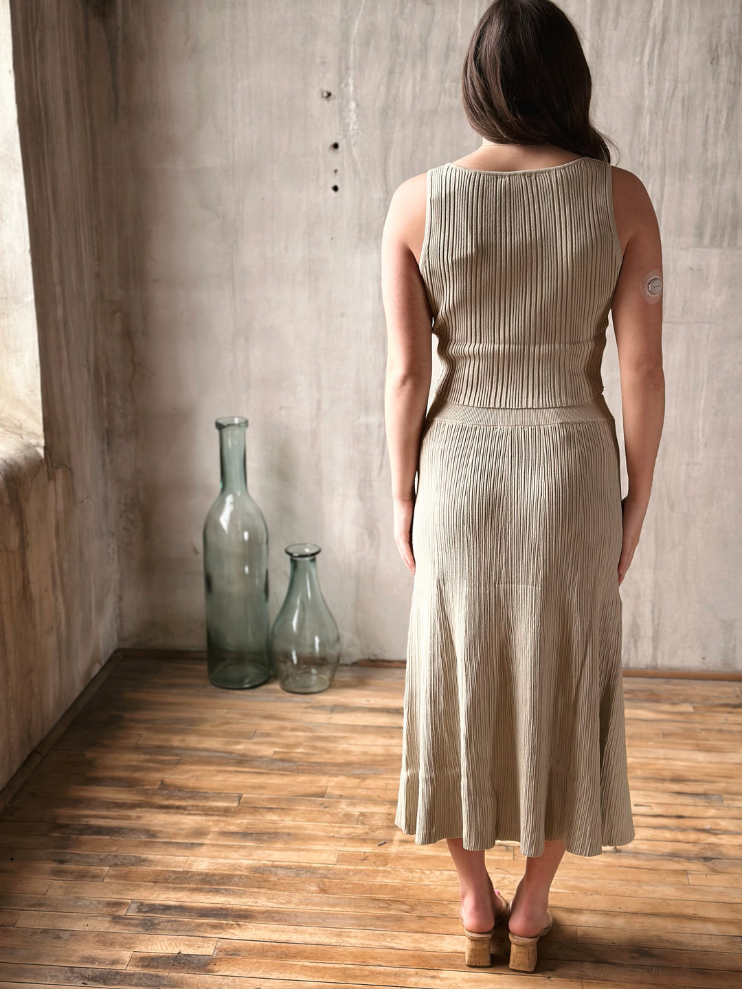 Woman wearing a beige skirt standing in a room with wooden floor and textured walls.