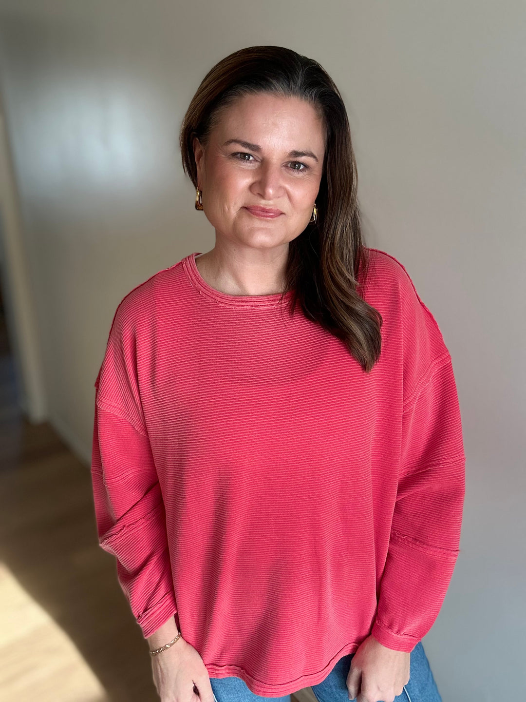 Woman wearing a pink sweater standing indoors with a neutral background