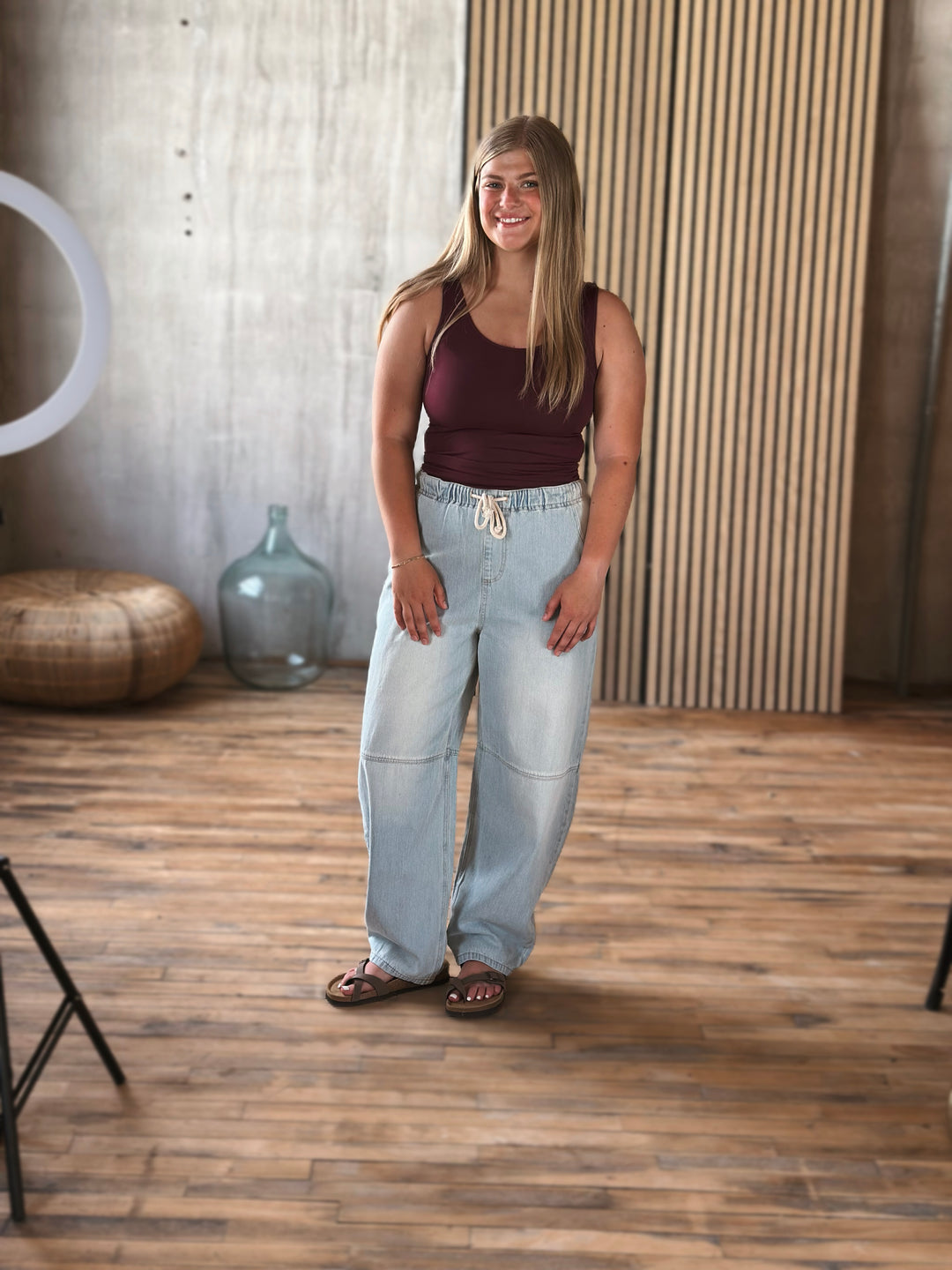 A woman wearing light washed barrel jeans with a jaw string at the waist. 