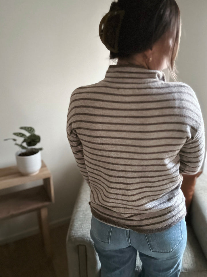 Person wearing a striped sweater and jeans in a room with a plant on a small table.