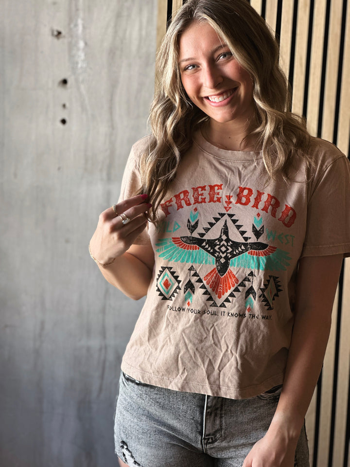 Front view of model wearing taupe t-shirt with colorful free bird design and writing