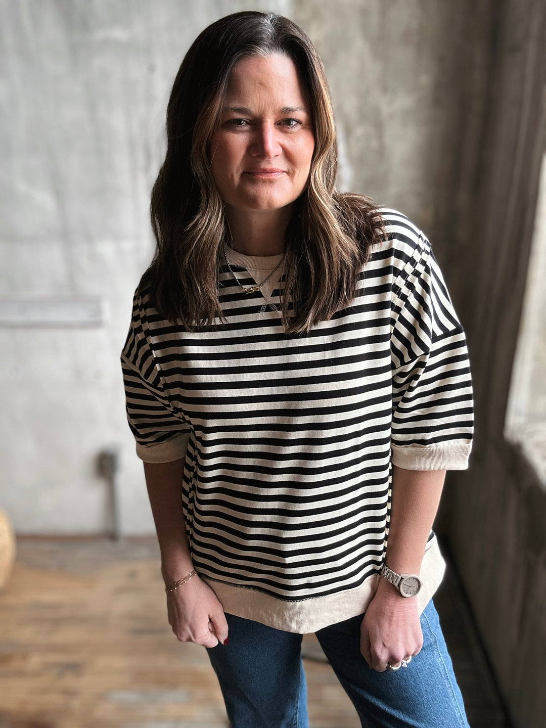 Woman wearing a black and white striped shirt and blue jeans indoors.