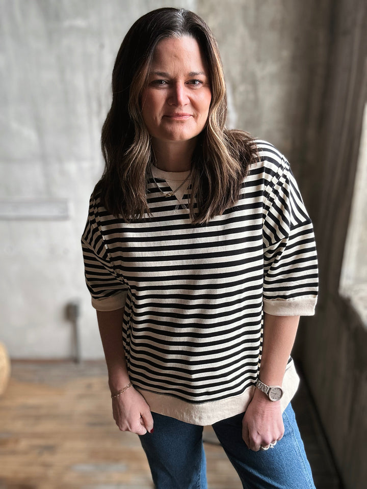 Woman wearing a black and white striped shirt and blue jeans indoors.