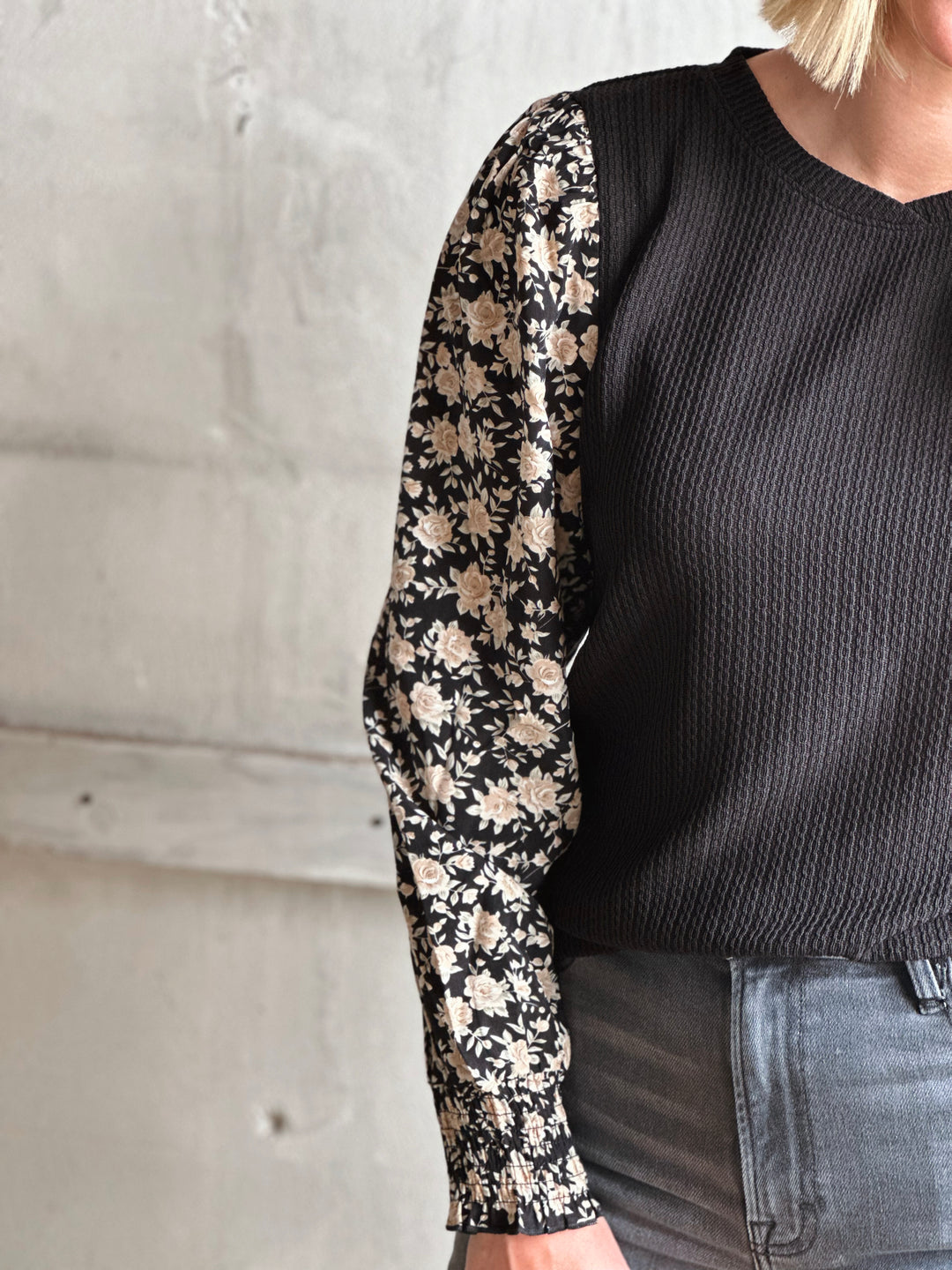 Person wearing a black sweater with floral sleeves against a neutral background