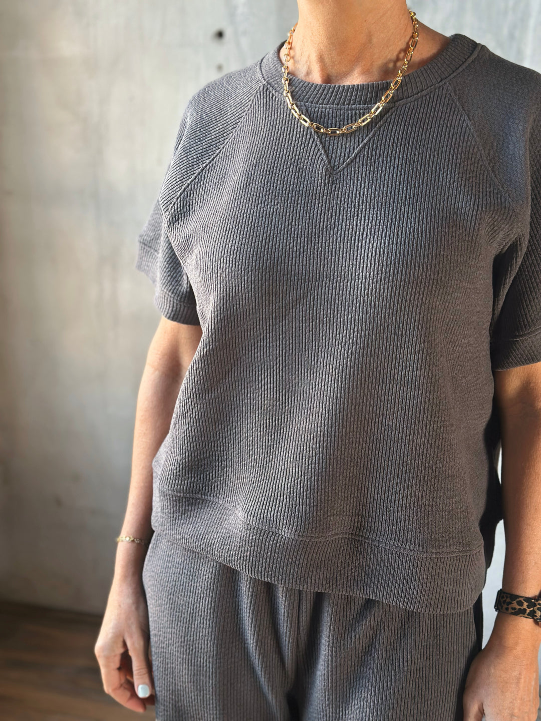 Person wearing a gray textured sweater and pants with a neutral background