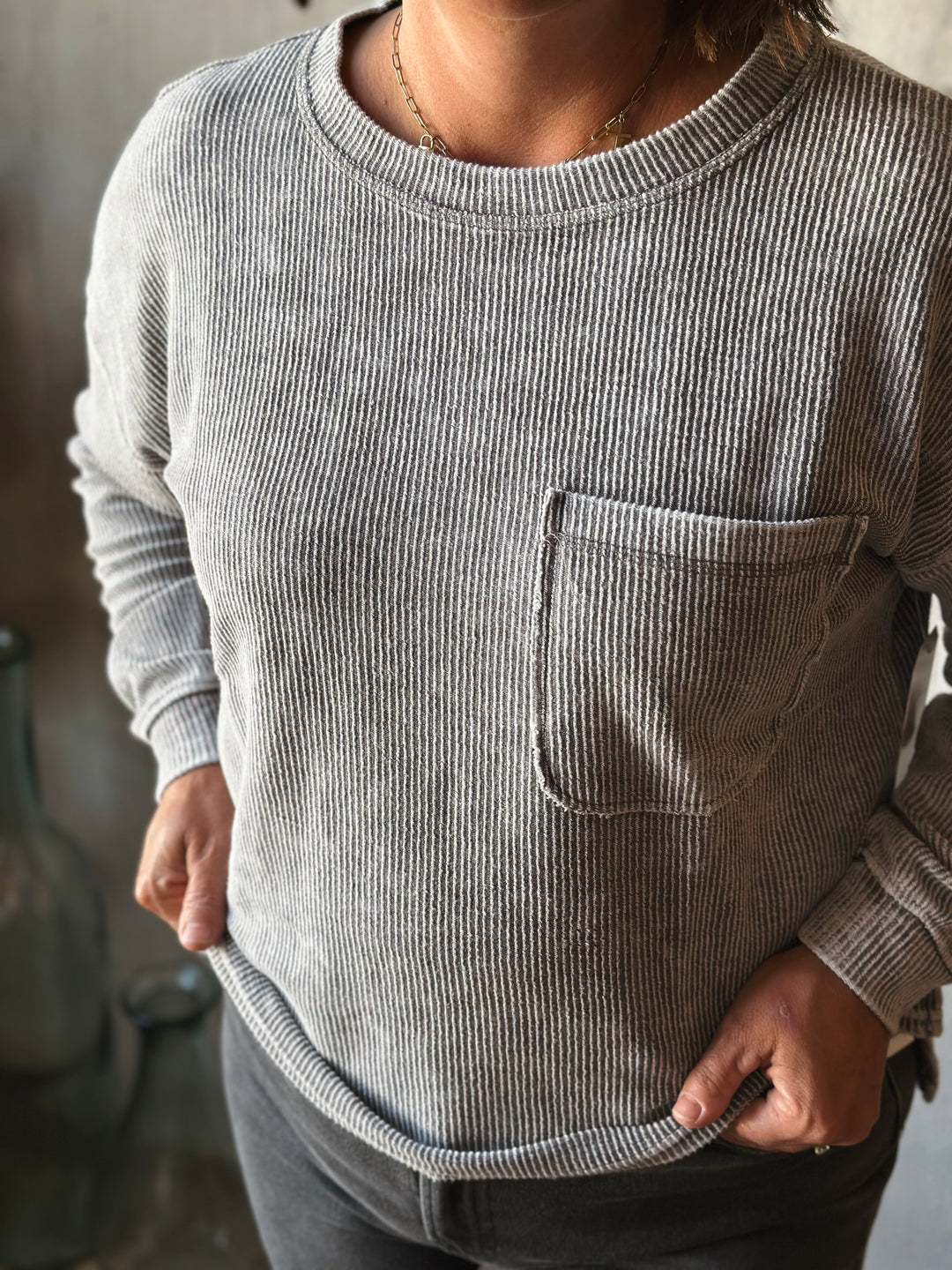 Person wearing a gray ribbed sweater with a pocket.
