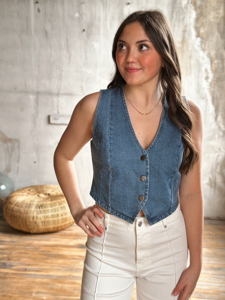Woman wearing a denim vest with buttons and white pants in a casual setting