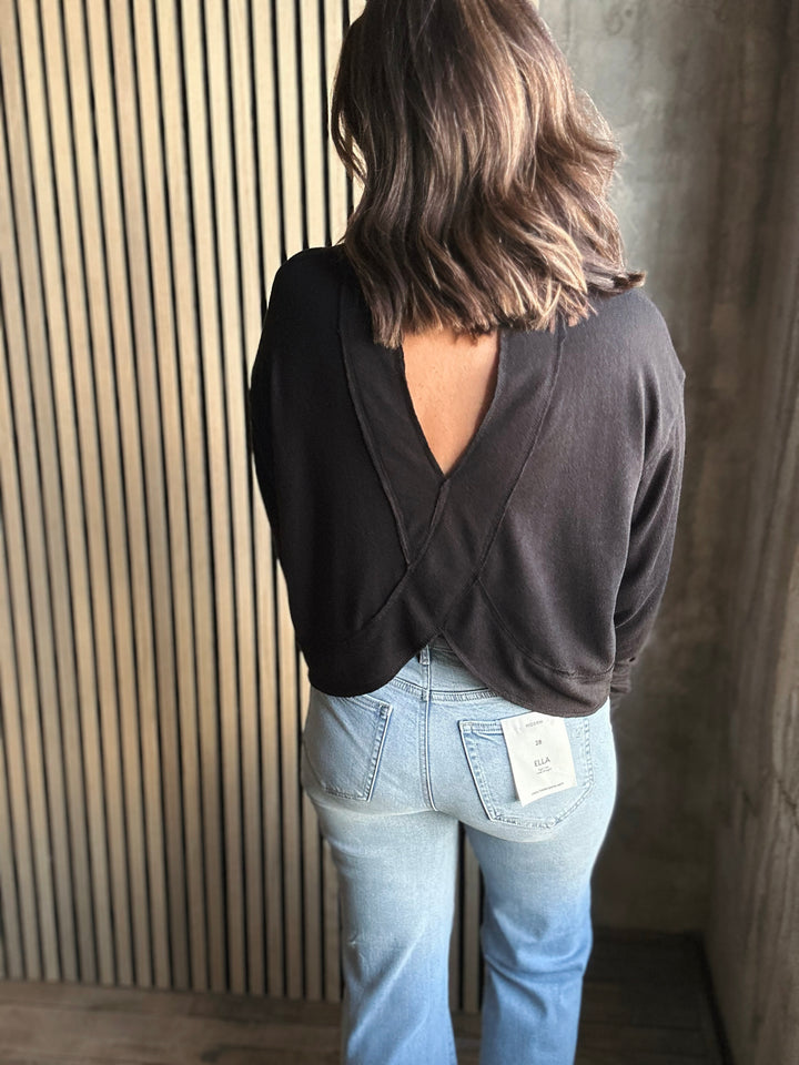 Person wearing a black open-back top and light blue jeans against a wooden slat wall.