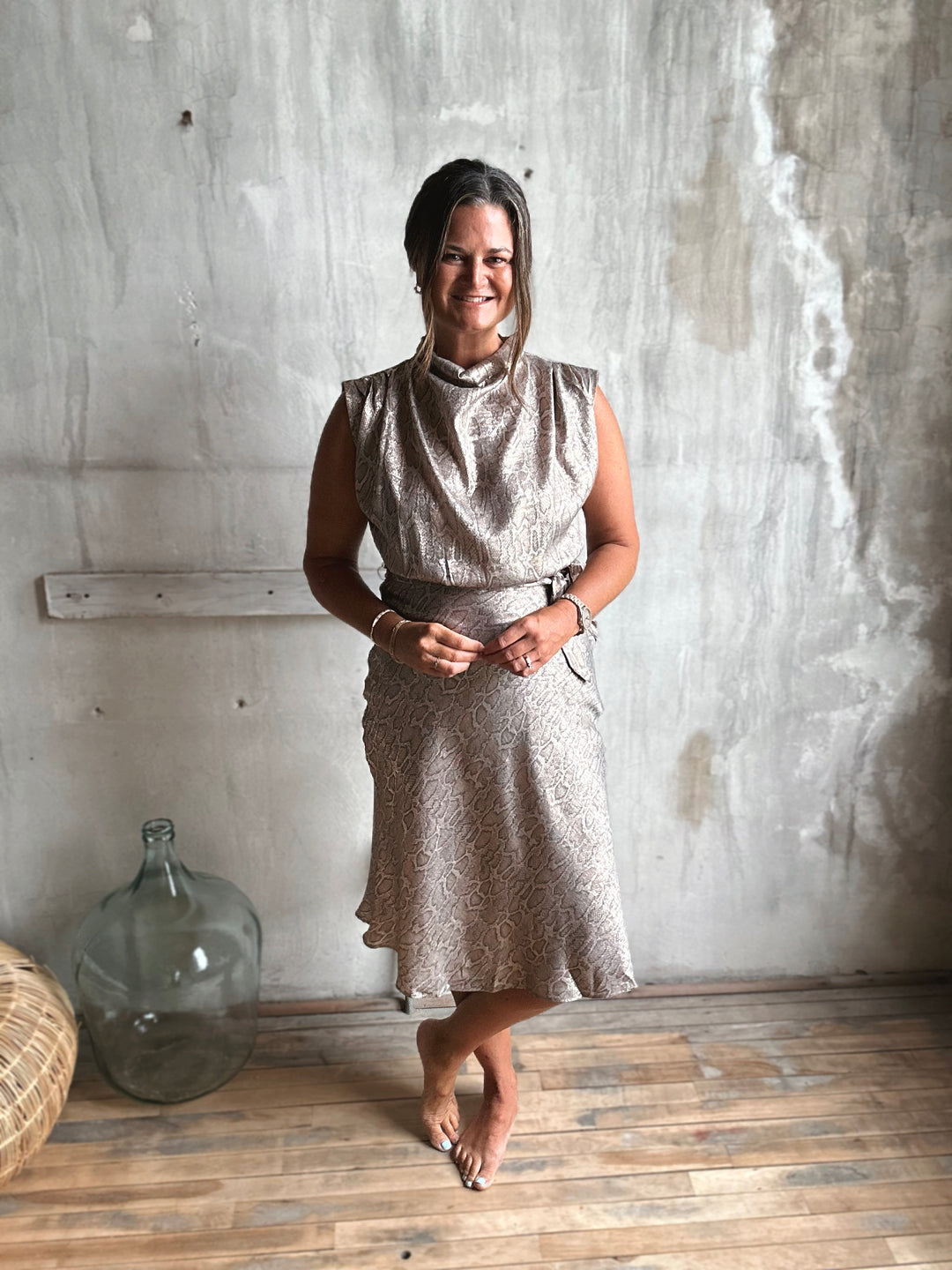 Woman in a patterned dress standing against a textured wall.