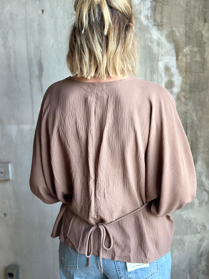 Person wearing a brown blouse with balloon sleeves against a textured wall.