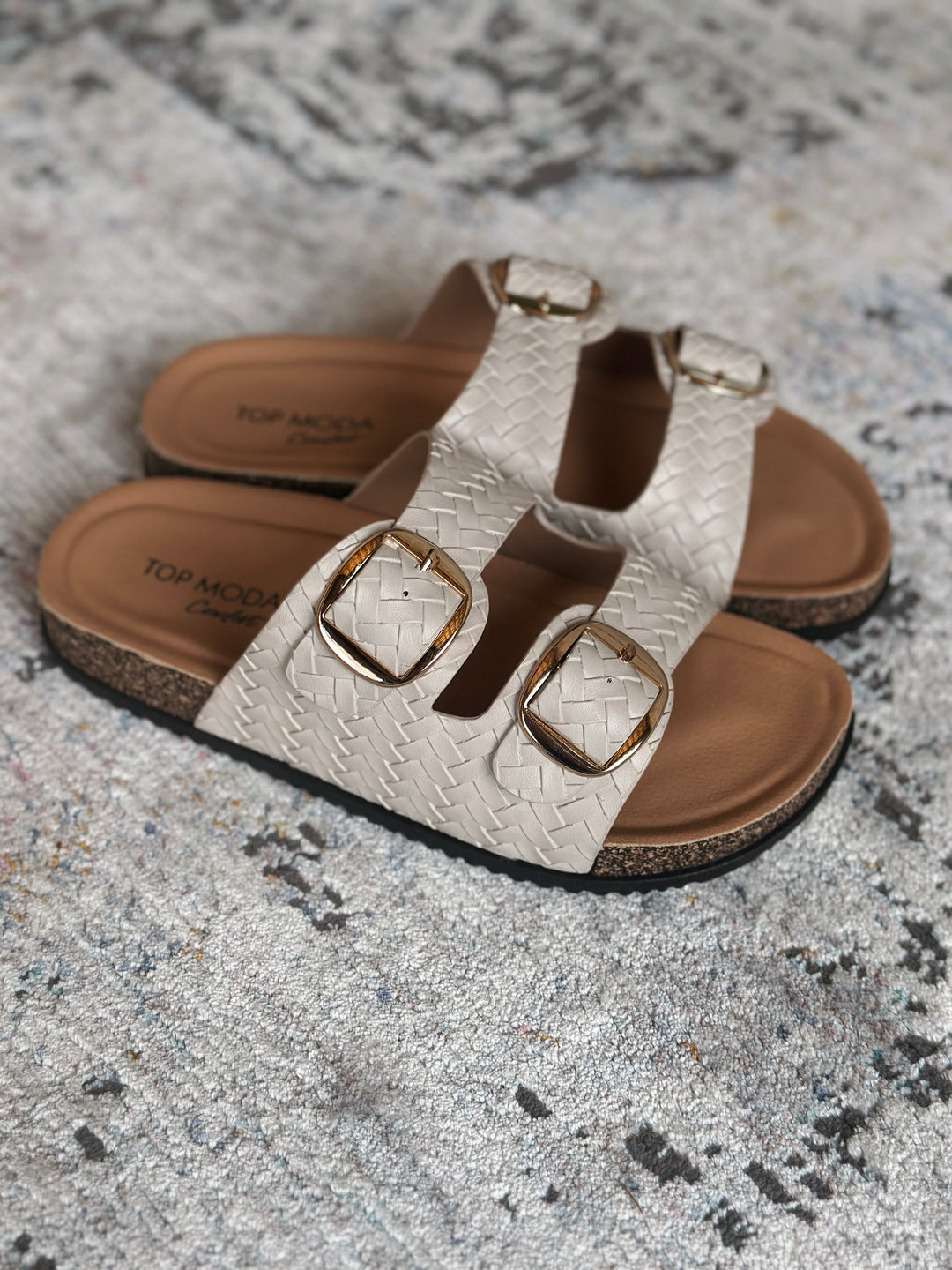 Pair of sandals with woven design and gold buckles on a textured surface.