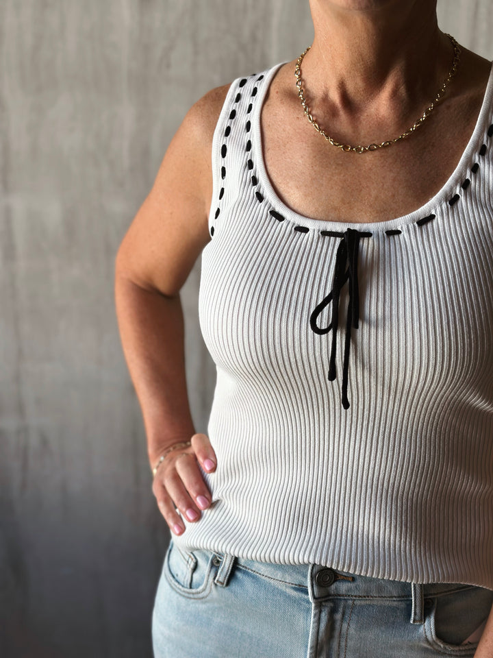 front view of sleeveless sweater knit tank features a flattering scoop neckline and a playful front tie detail. Cream top with black bow. 