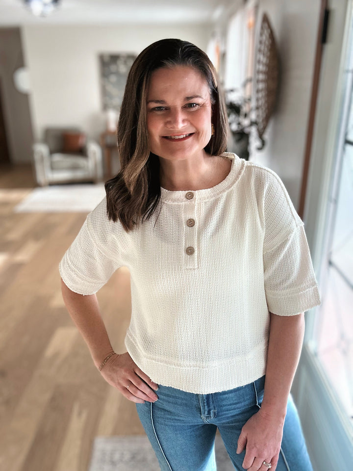 Woman wearing a white short-sleeve shirt and blue jeans indoors.