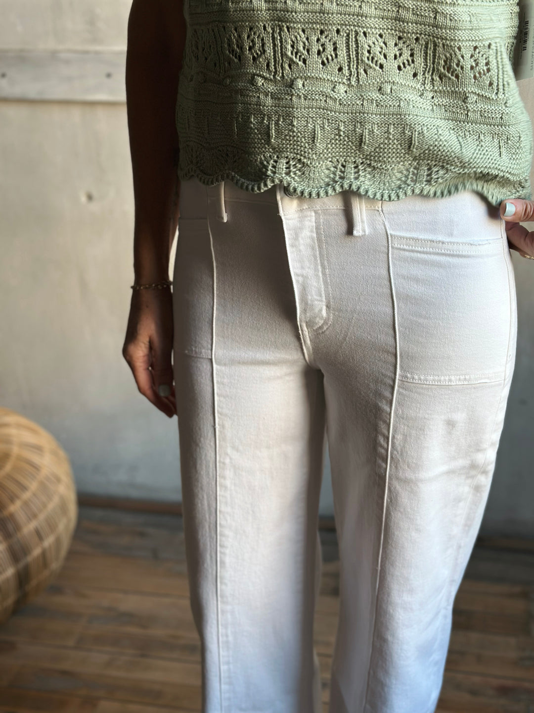 Person wearing a green knitted top and light-colored pants indoors.