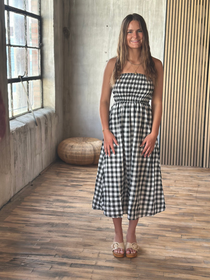 A woman wearing a black and white plaid strapless dress standing in a room with a wooden floor and textured walls.
