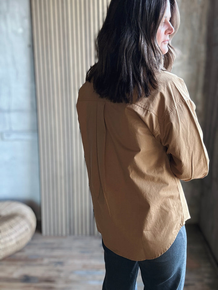 Person wearing a beige jacket standing indoors with a neutral background