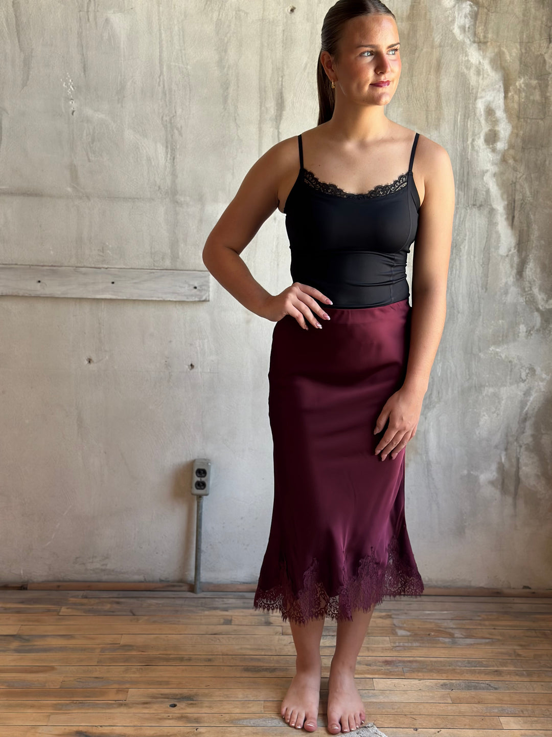 Woman wearing a burgundy satin midi skirt with lace hem and a black lace-trim cami