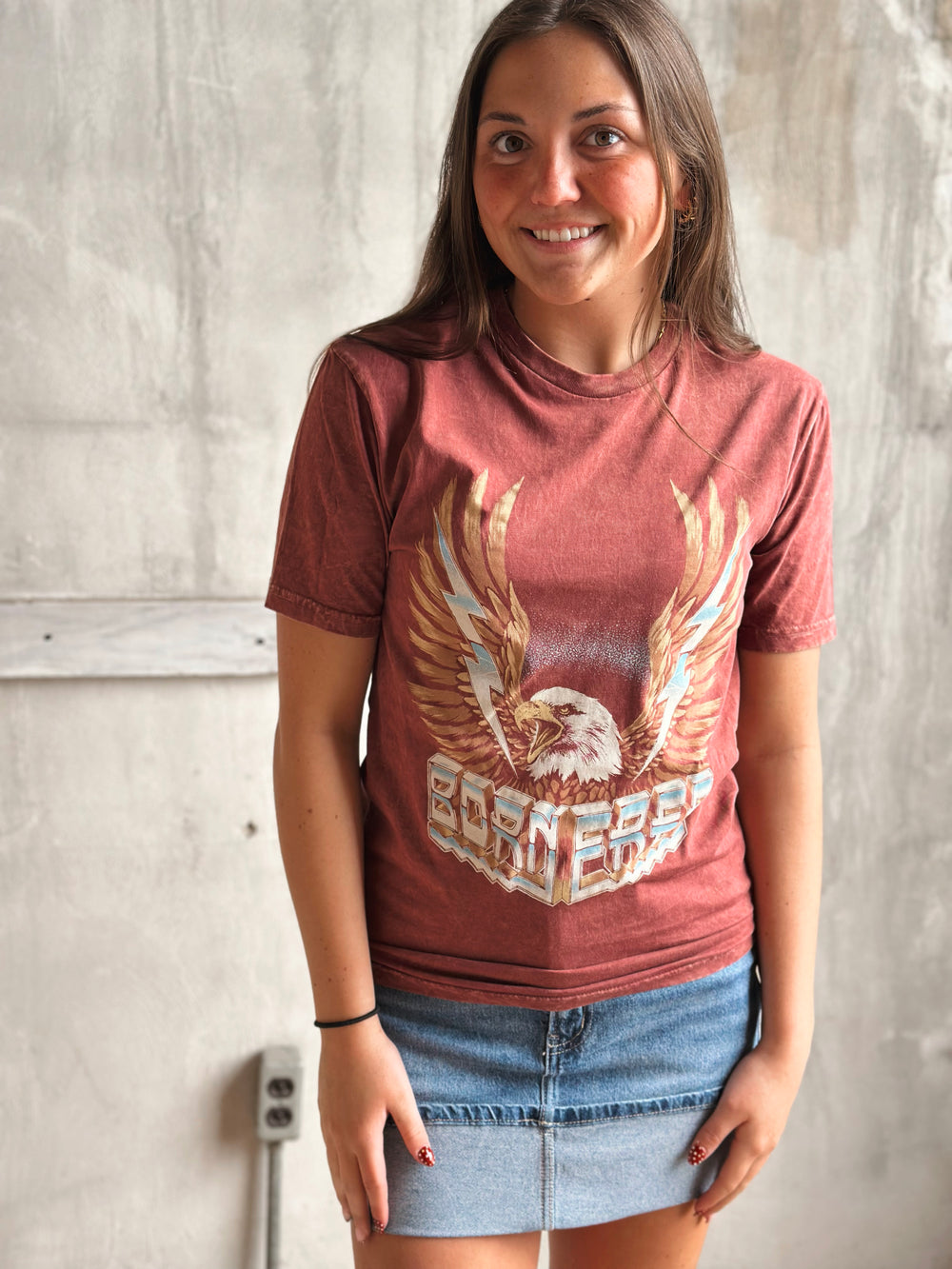 Woman wearing a red t-shirt with an eagle graphic against a plain wall.
