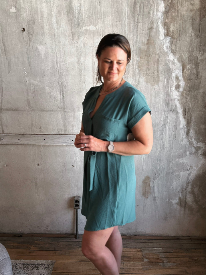 Woman wearing a teal dress standing against a textured wall.