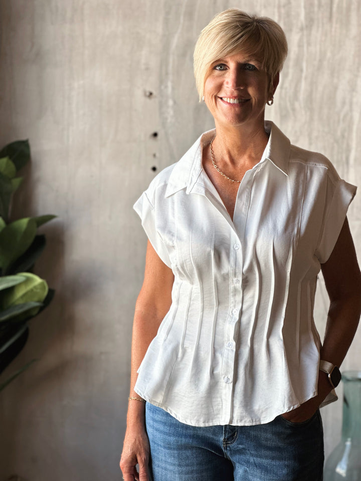 Woman wearing a white blouse and blue jeans standing against a neutral wall.