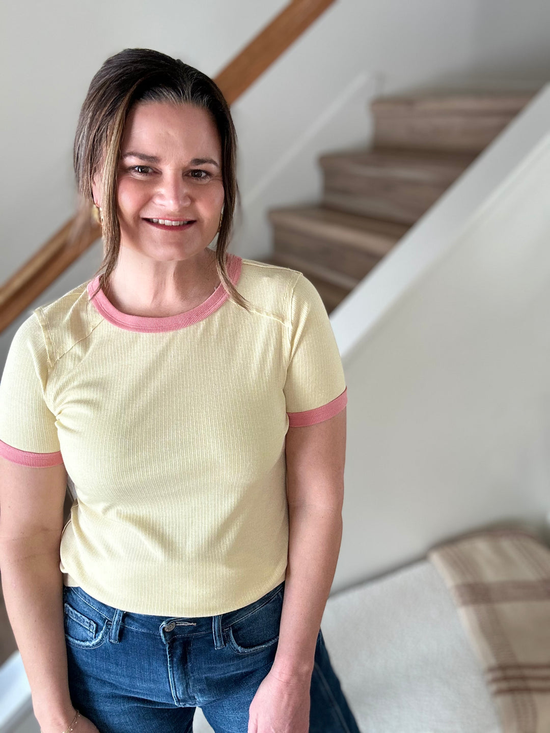 Woman wearing a yellow shirt with pink trim standing in a home setting.