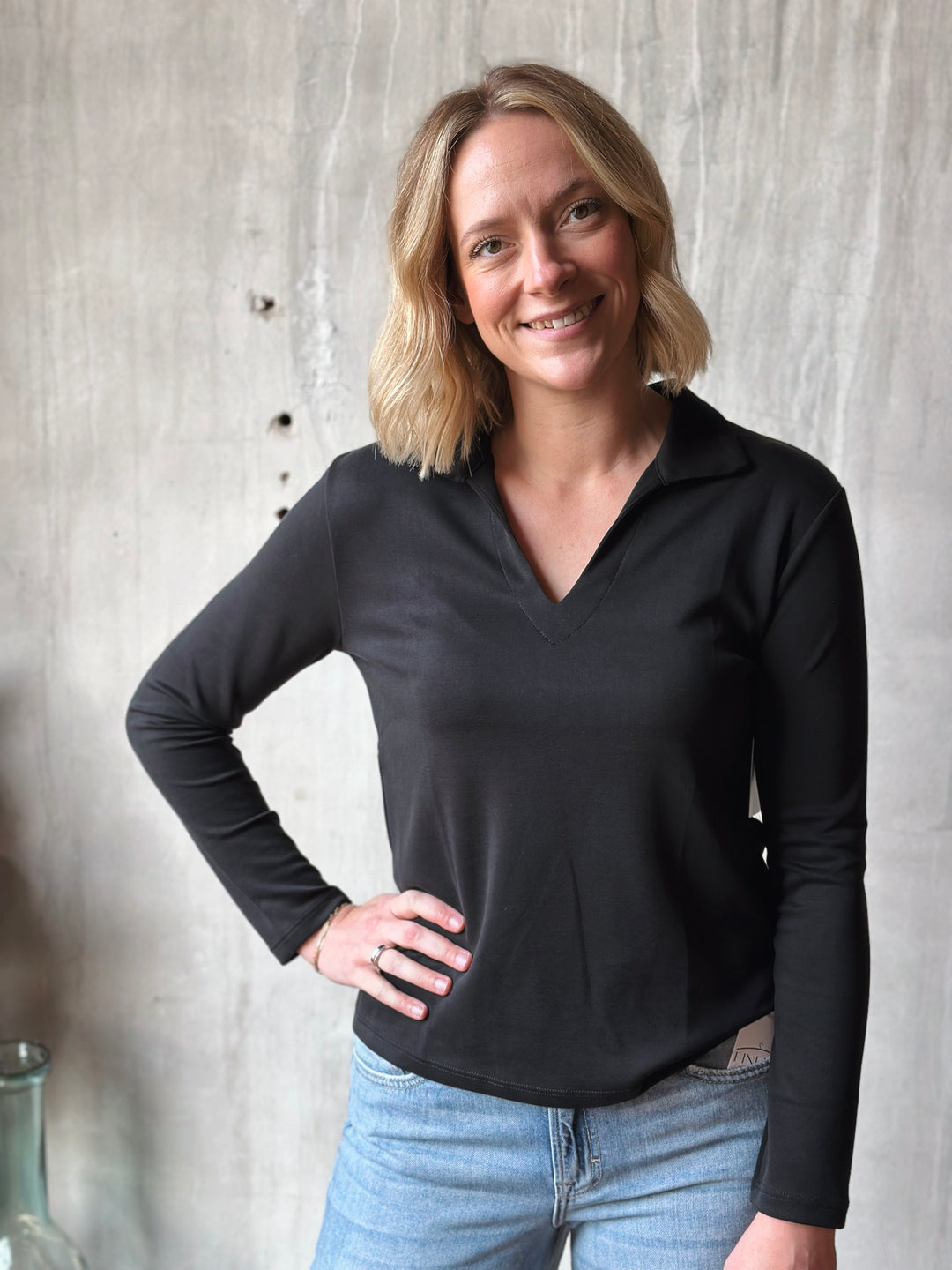 Woman wearing a black long-sleeve shirt and blue jeans against a neutral background