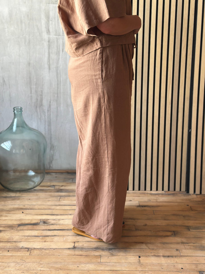 Person wearing a brown outfit standing in a room with wooden flooring and a large glass container.
