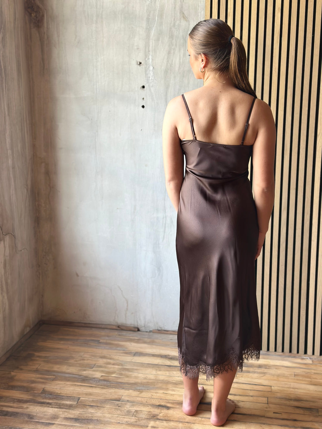 Back view of a chocolate brown satin slip dress with thin straps and lace hem