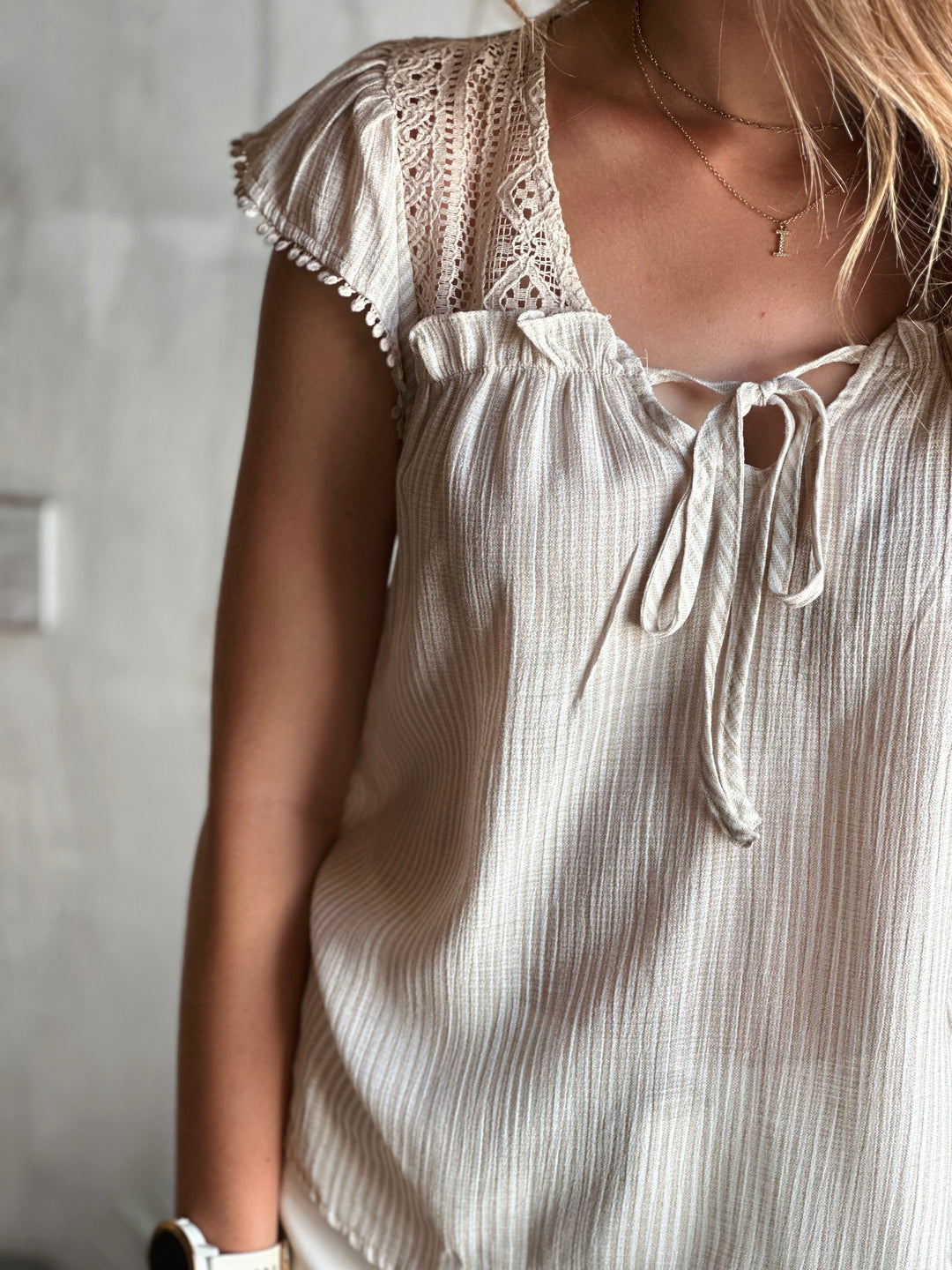 Front view of model wearing short sleeve with a tie neck line in light khaki color with striped texture and fabric design