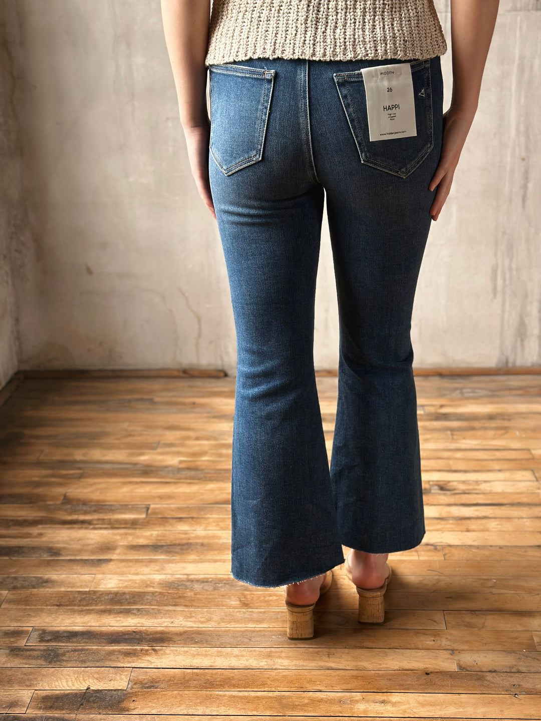 Person wearing blue flare jeans with a visible brand tag on a wooden floor.