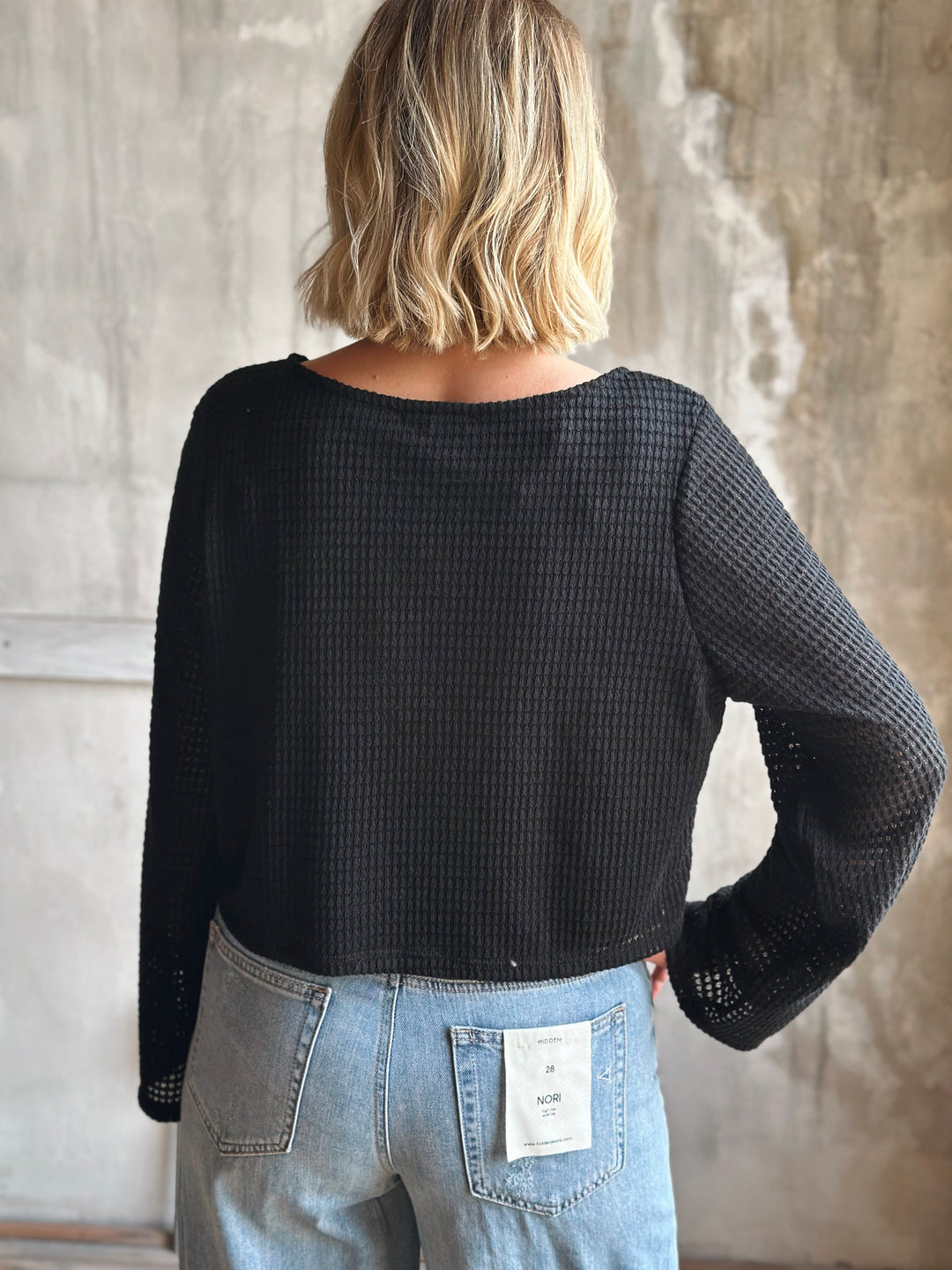 Person wearing a black textured sweater and blue jeans against a neutral background
