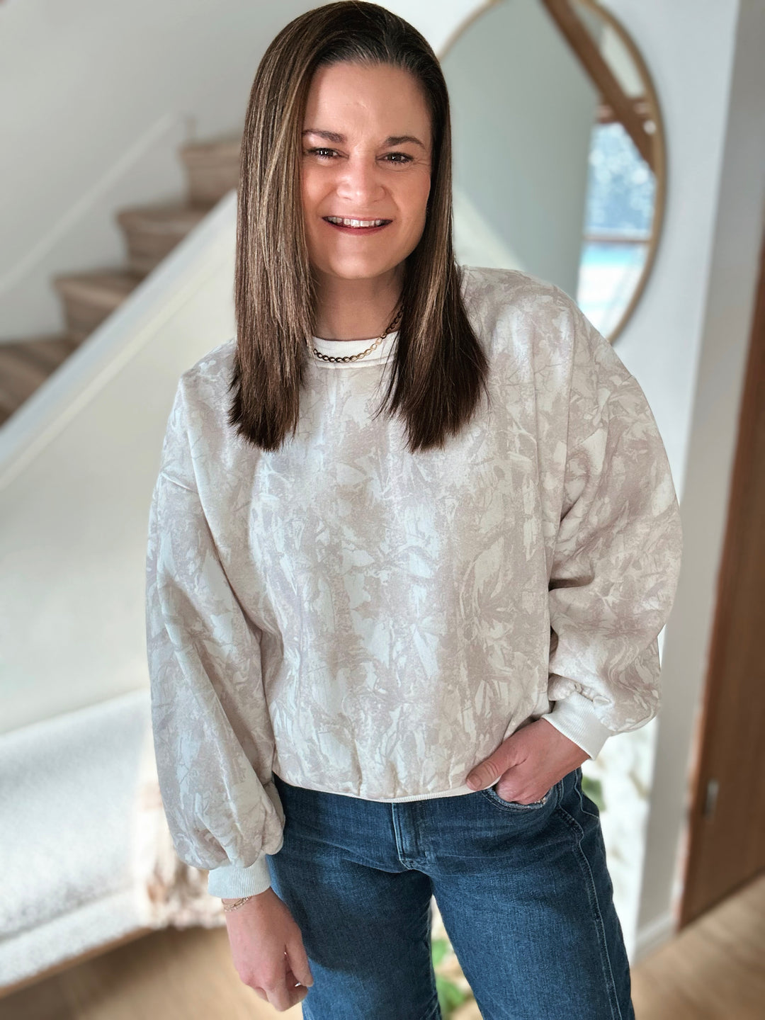 Person wearing a light-colored patterned sweater and blue jeans indoors.