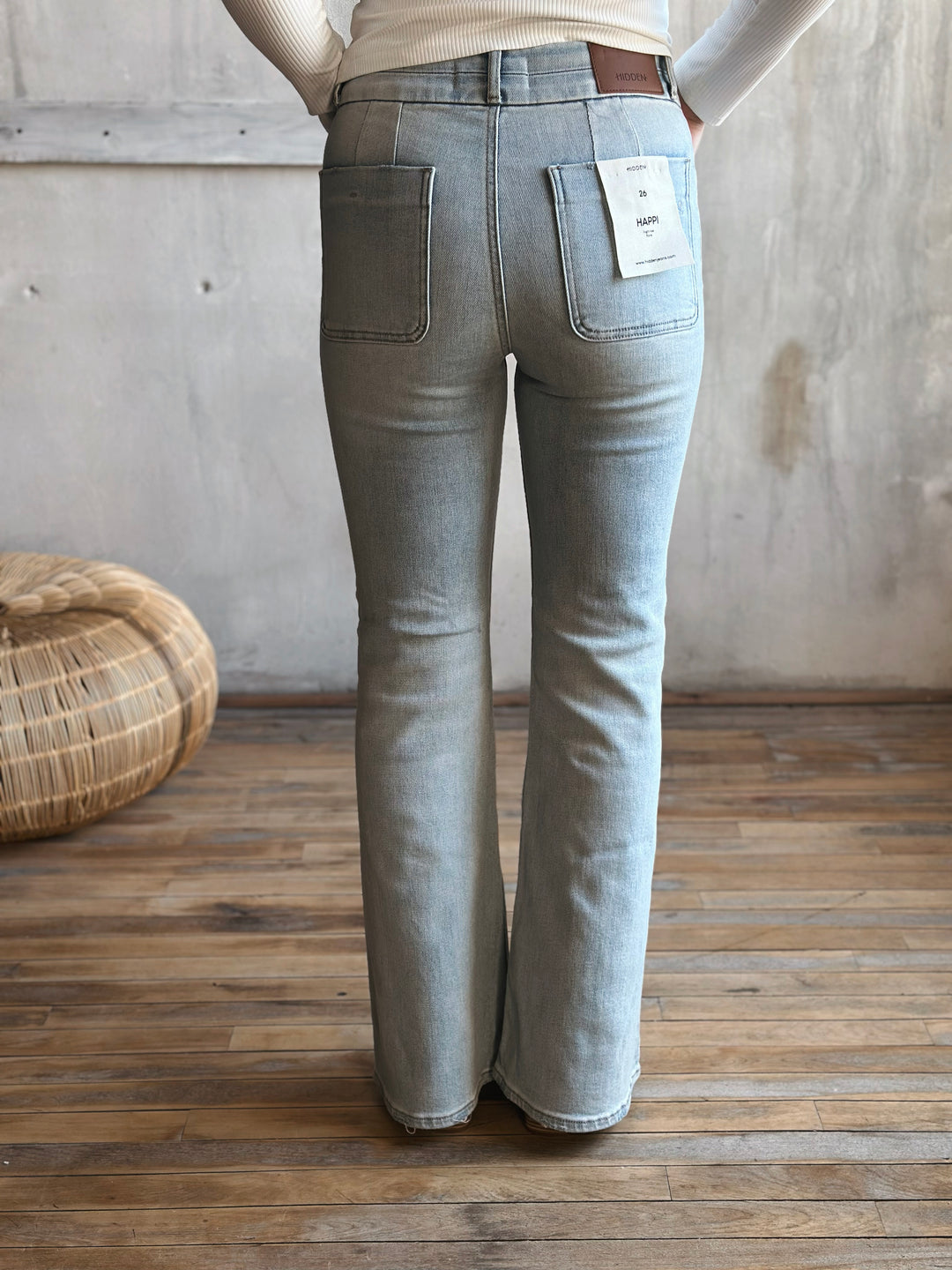 Person wearing light blue flared jeans with a wooden floor and woven basket in the background
