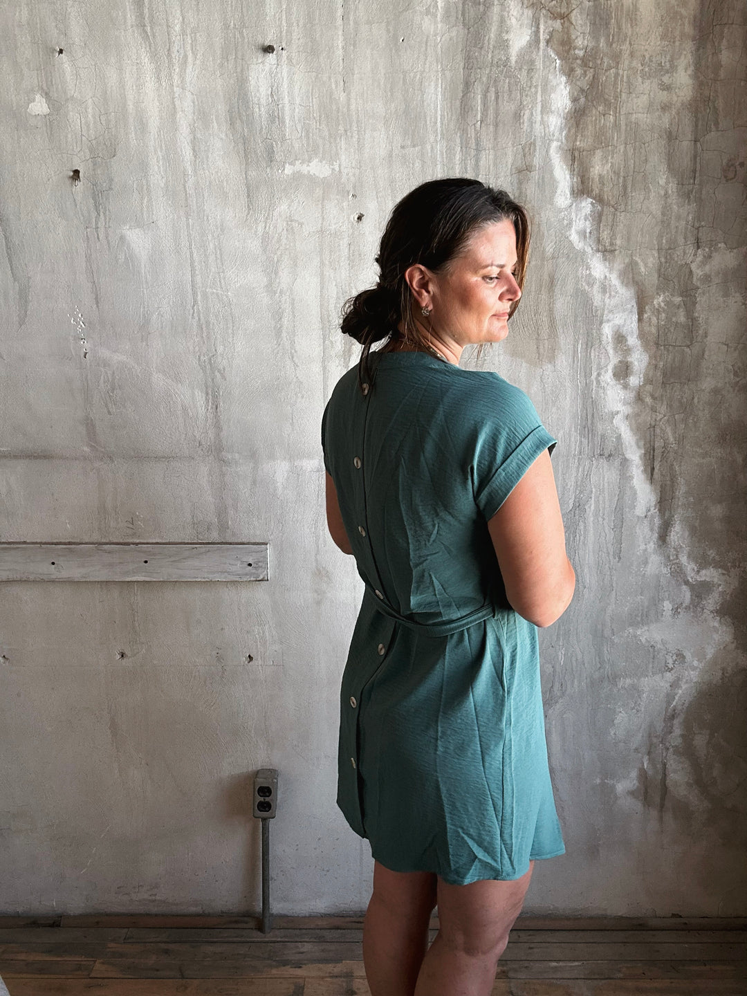 Woman wearing a teal dress with buttons going down the back. 