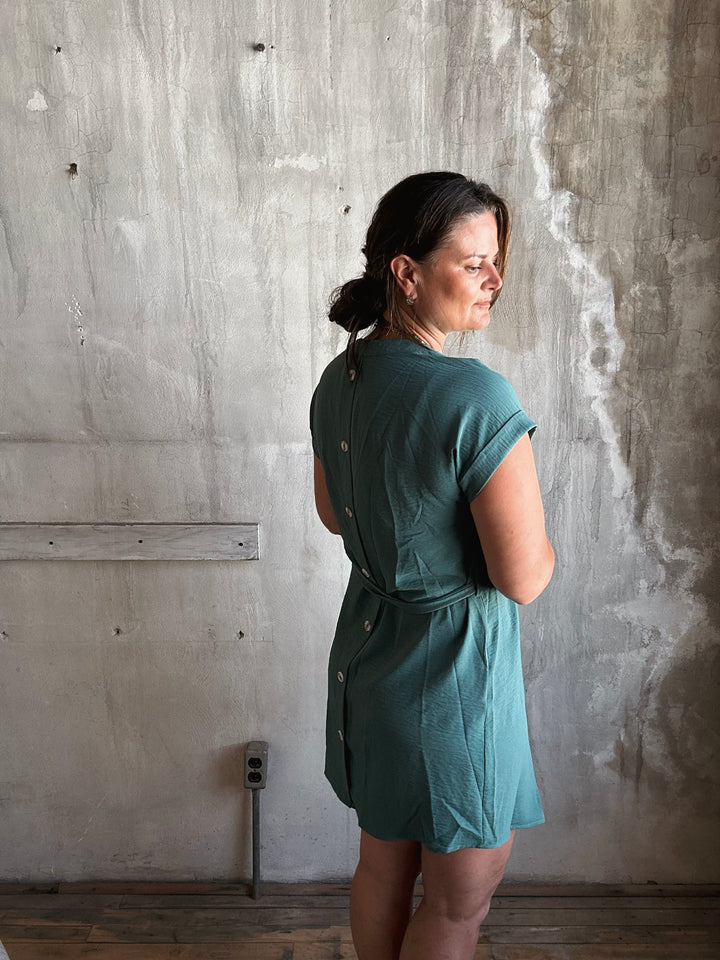 Woman wearing a teal dress with buttons going down the back. 