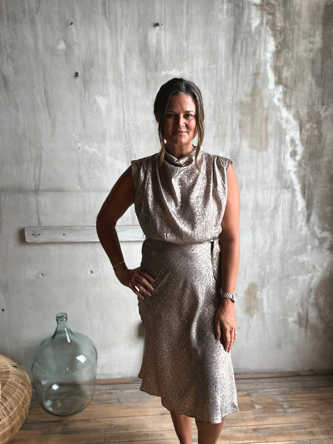 Woman wearing a sparkly dress standing against a textured wall.